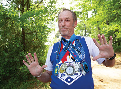 John Crosby showcasing various medals he's won at running events.